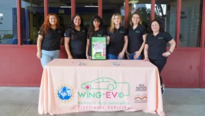 A group of women standing in front of a table with a Wing-EV sign.