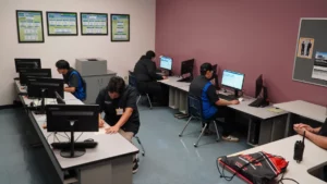 Four individuals working on desktop computers in an office with informational posters on the wall.