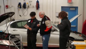 Three individuals reviewing a vehicle in an auto repair shop.