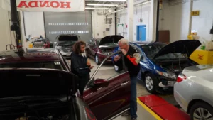 Two individuals having a conversation in an automotive workshop with several cars in the background.