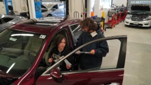 Two mechanics reviewing a document beside a red car in an auto repair shop.