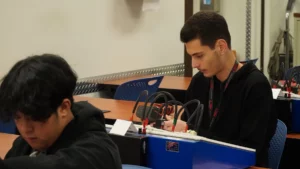 Two individuals working on electronic equipment in a classroom setting.