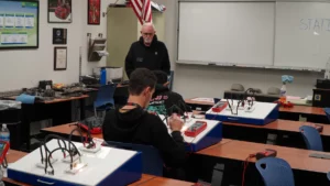An instructor oversees students working on electronic circuit projects in a classroom.
