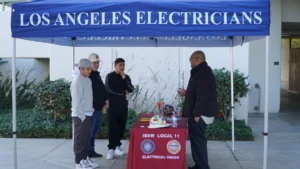 Three individuals standing under a tent labeled "los angeles electricians," interacting with a representative at an informational booth.
