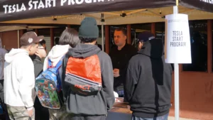 Group of individuals inquiring about the tesla start program at an information booth.