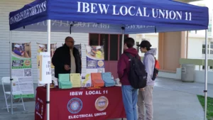 Individuals stand at an ibew local union 11 information booth with educational materials on display.