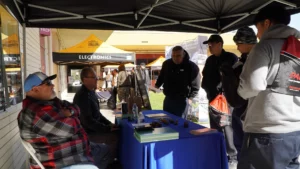Attendees engage in conversation at an outdoor electronics event booth.
