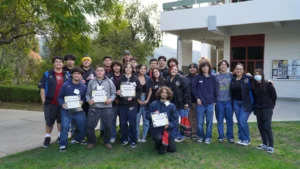 A diverse group of students posing together outdoors, with some holding certificates.