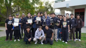 Group of students posing with trophies outdoors.