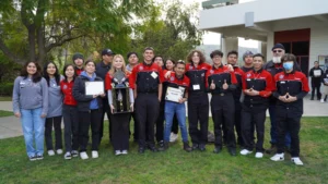 A group of students in various uniforms, some holding awards, posing for a photo outdoors.