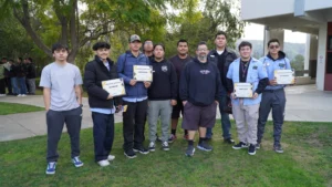 A group of male students and an instructor standing outdoors, holding certificates of achievement.