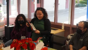 Woman reads a greeting card at a gathering with people and poinsettia plants on the table.