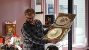 Man presenting decorative plates at an event while another person looks on.
