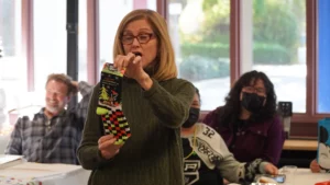 A woman holding up a christmas sock while speaking to an audience indoors.