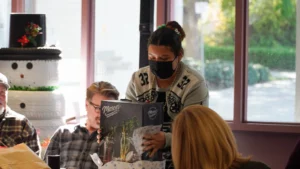 A masked server taking an order from customers at a restaurant.