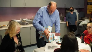 A man unwrapping a gift at a gathering while others watch.