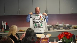 Man holding up a holiday-themed shirt at an office party.