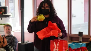 A person wearing a mask holding a yellow mug and red tissue paper at a social gathering.
