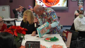 Man in a colorful shirt presenting a lottery ticket to a smiling woman at a festive gathering.