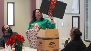 A woman holding a gift aloft at an office party while colleagues look on.