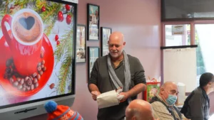 A man giving a presentation in a room with an image of a festive cup of coffee displayed on a screen.