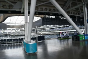 An empty stadium concourse area with structural columns, seating visible in the background, and a super bowl advertisement sign.