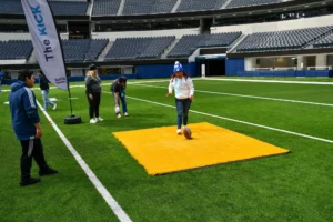 A person prepares to kick a football on a yellow mat at an indoor stadium event.