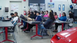 Group of students seated at tables in a technical workshop classroom, attentively listening to a lecture.