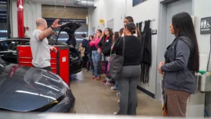 A group of people attending a car maintenance workshop in a garage setting.