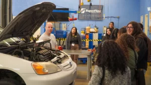 Automotive instructor explaining engine mechanics to a group of students in a workshop.