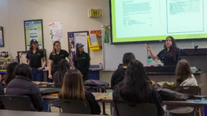 Four women presenting in a classroom while students listen.