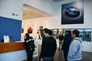 Customers standing at a reception desk in a bmw dealership lobby with automotive displays and brand logos on the wall.