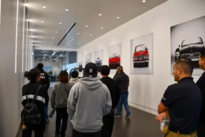 People viewing car displays and photographs in a modern showroom with white walls and overhead lighting.