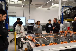 Students and an instructor discuss electric vehicle components in an automotive workshop.