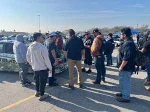 A group of people congregating around a vehicle in a parking lot during the day.