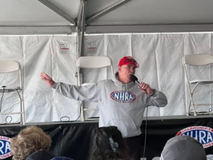 A person wearing an nhra sweatshirt speaks into a microphone in front of an audience.