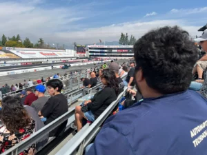 Spectators seated on bleachers at a drag racing event, focusing on the track ahead.