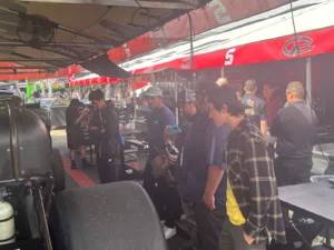 A group of people gathered under a tent at a racing event, possibly observing or waiting for activities to commence.