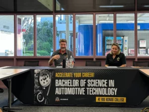 Two people sitting at a table during a presentation about a bachelor of science in automotive technology at rio hondo college.