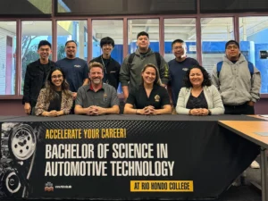 Group of students and instructors smiling behind a banner reading "bachelor of science in automotive technology at rio hondo college.