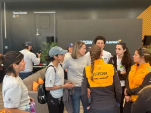 Group of people engaged in a conversation at a mclaren event, with some wearing mclaren branded clothing.