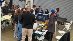 A group of people interact with representatives at a job fair. Several information tables and booths are set up, including one for Los Angeles County Sanitation Districts.
