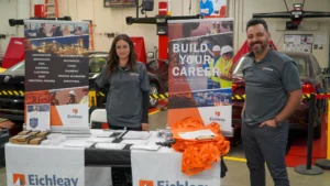 Two Eichleay representatives stand behind a table with brochures, orange bags, and banners promoting career opportunities in a workshop setting.
