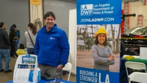 A person in a blue jacket stands next to a Los Angeles Department of Water & Power booth with brochures and a banner promoting careers, featuring a woman in a hard hat.