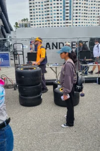 A woman and a man in a high-visibility vest inspect racing tires at an outdoor motorsport event.