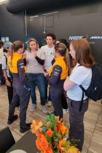 A group of people in casual and team apparel engaging in a conversation in a mclaren racing team tent.