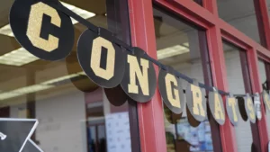 A black and gold banner spelling "CONGRATS" is hung in front of a building with red framing.
