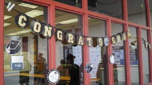 A string of decorations spelling "CONGRATS GRAD" hangs across red-framed glass doors, with graduation-themed cutouts and posters visible in the background.
