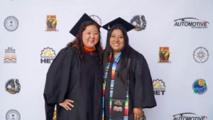 Two individuals in graduation caps and gowns smile for a photo in front of a backdrop featuring logos from Rio Hondo College and its programs.