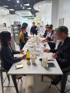 Group of people participating in a workshop at a modern table, blending scents in a brightly lit perfume lab.